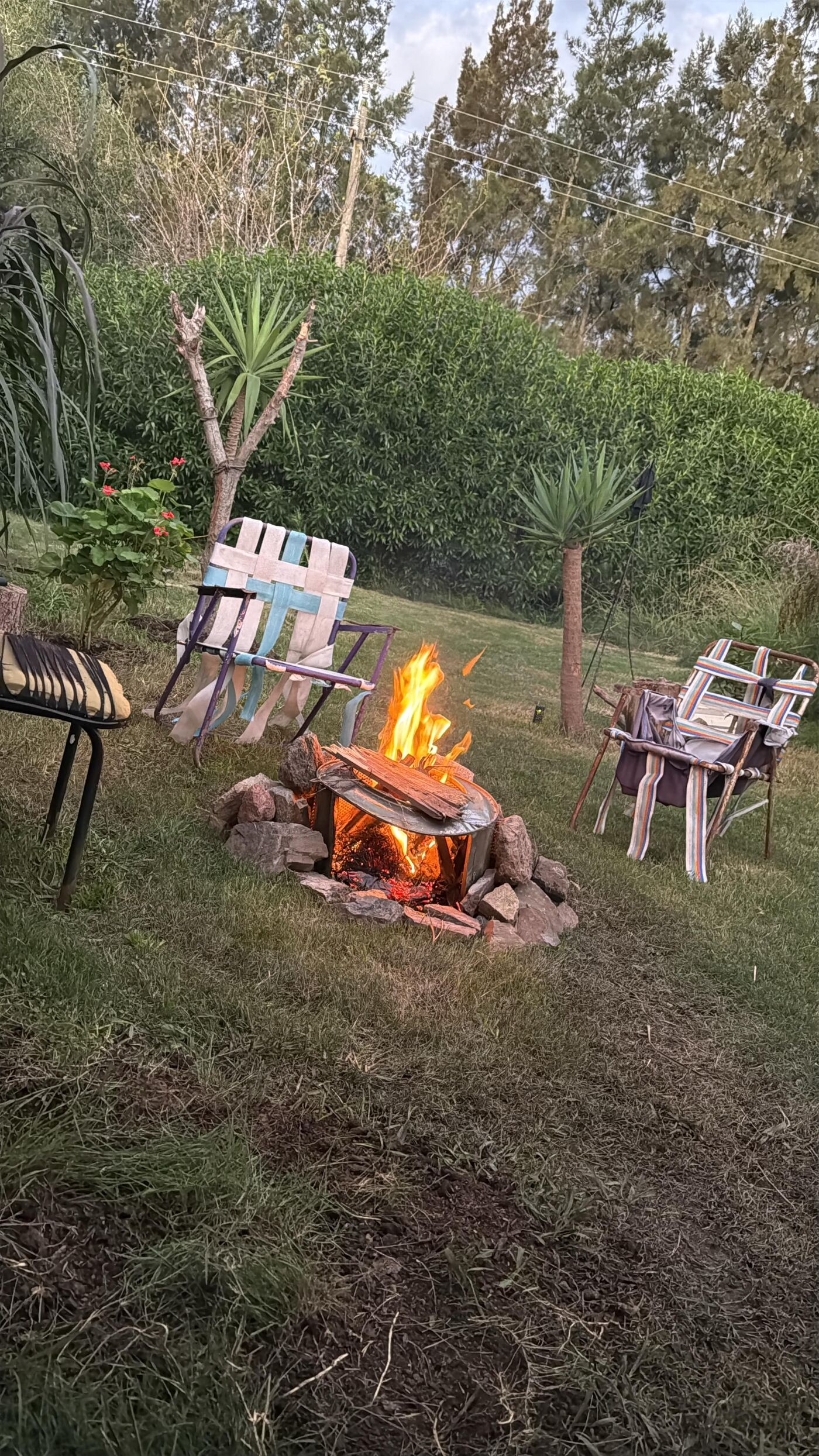 The washing machine drum fireplace at Tierra de Sueños, surrounded by mismatched garden chairs at dusk.